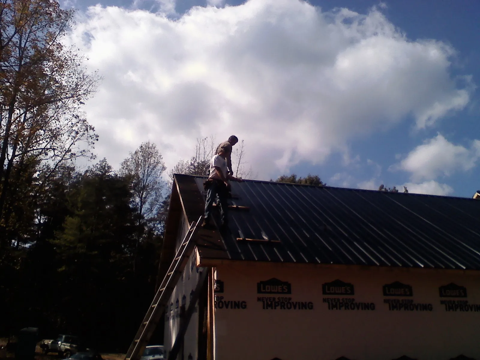 Roofer fastening dark metal panels high against a cloudy sky, from a Roof Inspection job in Gypsum