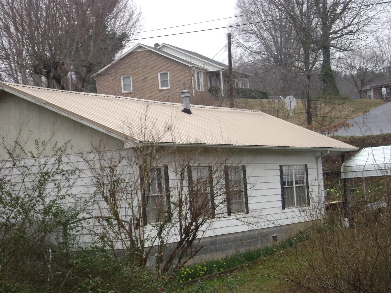 Tan metal roof on a white sided house set into a hillside — Commercial Roofing by Roofing Brothers in Gypsum